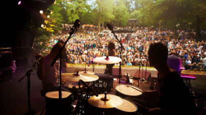 Band, music festival and stage in outdoors, event and party or energy for freedom on vacation. People, back and concert or rave, audio and song for fun crowd and musicians with instruments for show.