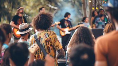 A group of people are enjoying a live music performance at an outdoor music festival. The focus is on the crowd, who are all looking at the stage.